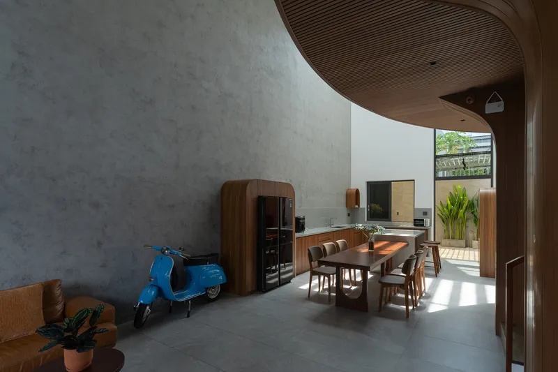 Living and dining space with blue scooter beside polished concrete wall under curved timber ceiling