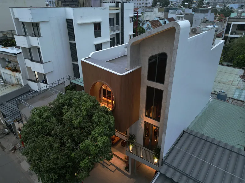 Elevated view of the white facade with timber-clad curved window and circular opening at dusk