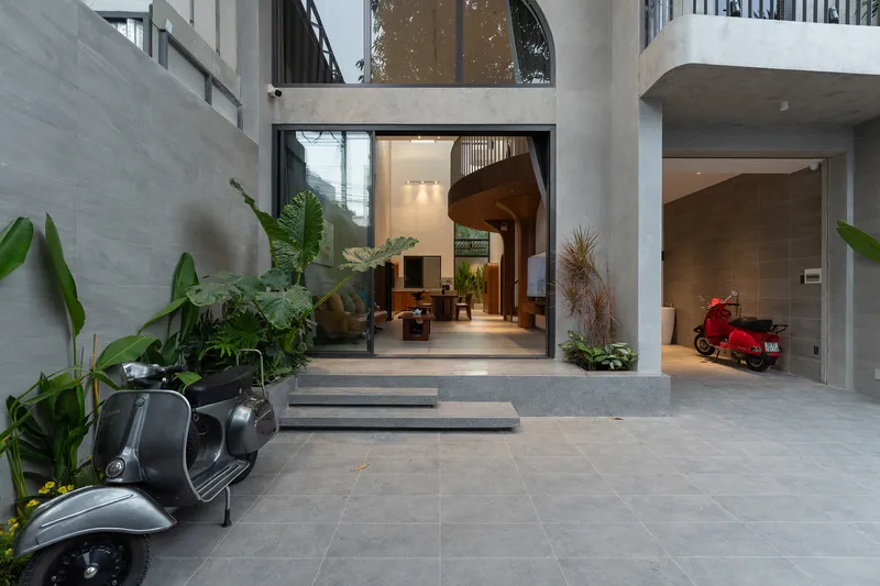 Ground-level courtyard with concrete pavers, planted beds, and motor scooters beneath glazed entry