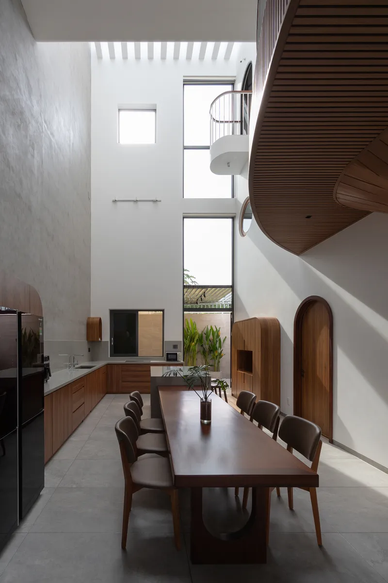 Vertical window stack illuminating dining table beneath suspended pendant and curved timber balcony edge