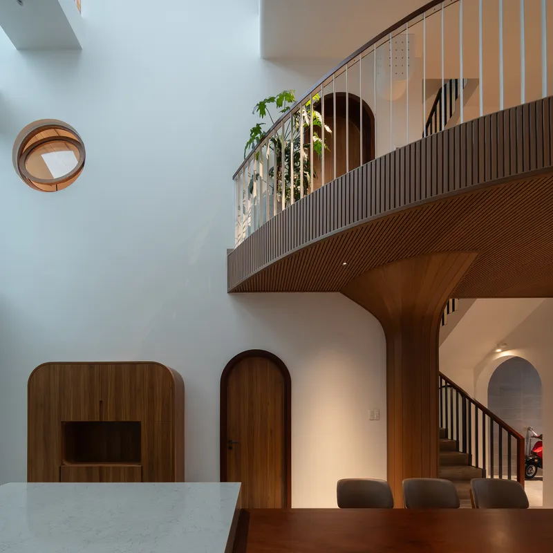 Curved timber balcony with vertical slat cladding suspended above arched doorways and dining area