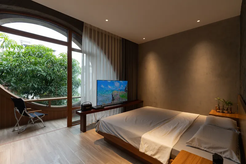 Bedroom with low timber bed and arched glazing opening to a planted terrace