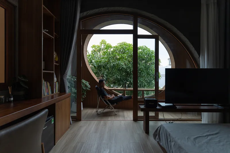 Circular window with occupant seated in a chair overlooking treetops