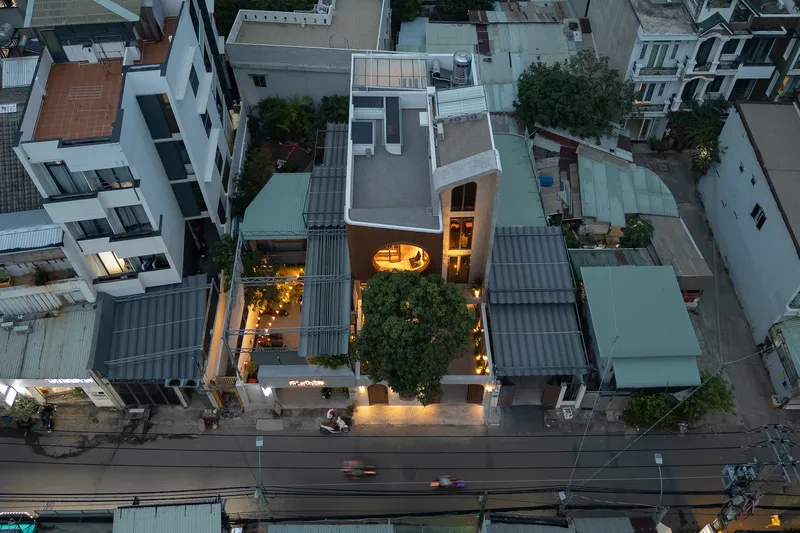 Aerial view at dusk showing the narrow house wedged between neighboring structures with interior lights glowing