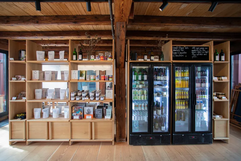 Retail wall with open timber shelving and glass-door refrigerators flanking a dark timber column