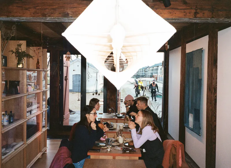 Narrow dining area with exposed timber beams and a large diamond-shaped pendant light over seated guests