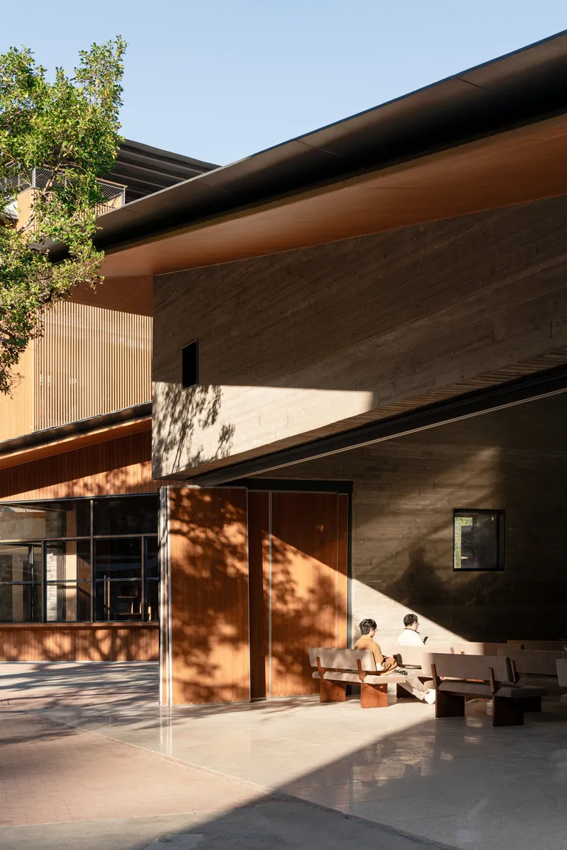 Covered outdoor area with concrete walls and dappled tree shadow falling across timber doors