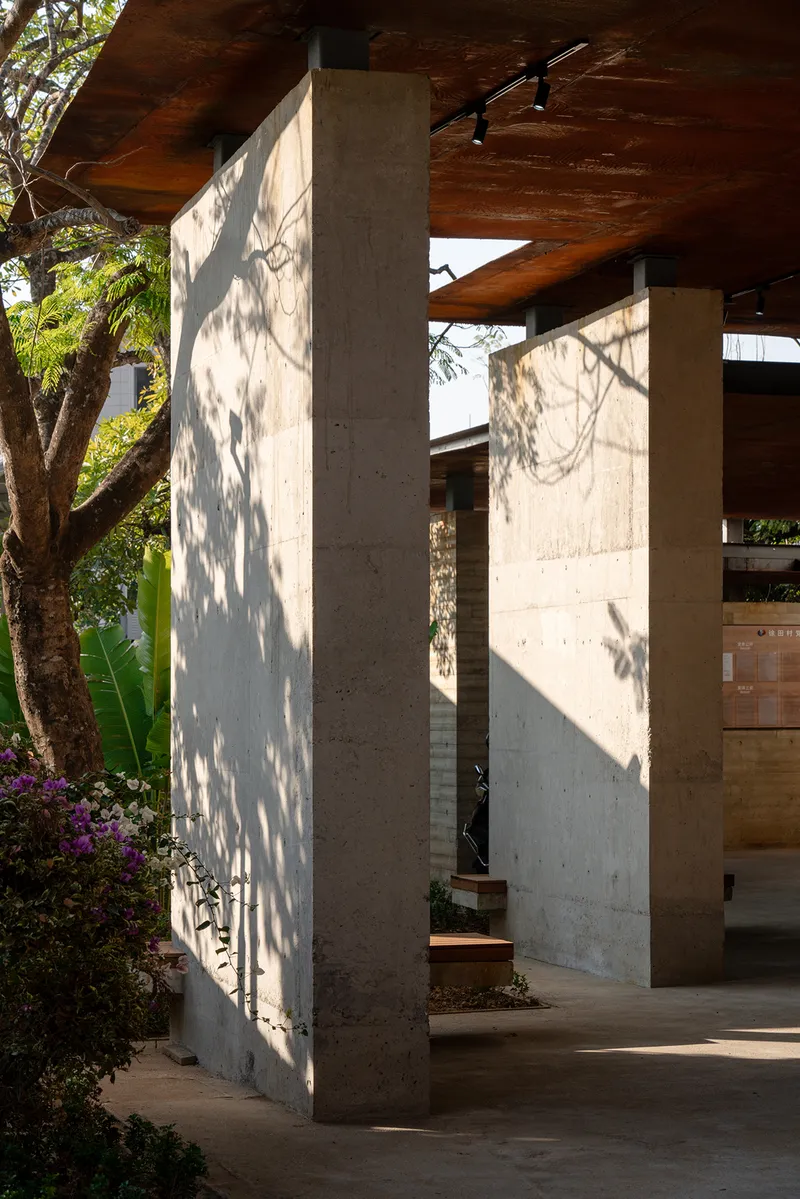 Concrete columns with dappled tree shadows beneath a timber plank soffit at an exterior covered passage