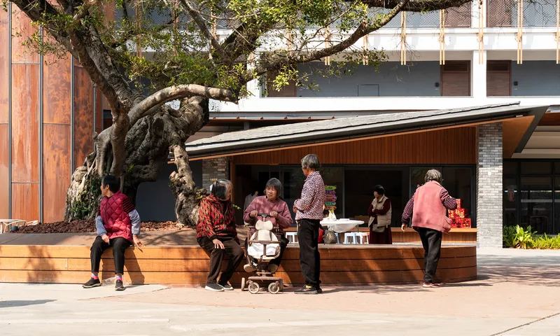 Timber deck and bench seating beneath an overhanging roof where community members gather under an old tree
