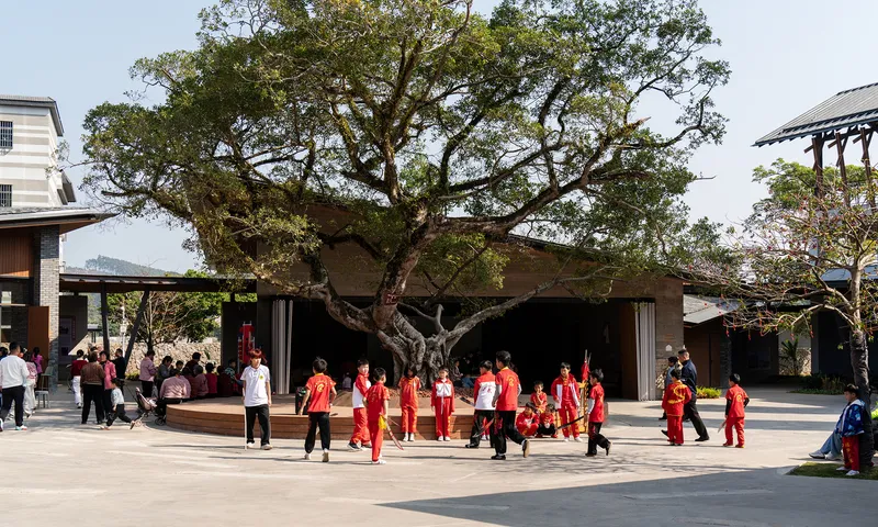 Low pavilion sheltering beneath a large tree with performers in red gathered on the plaza