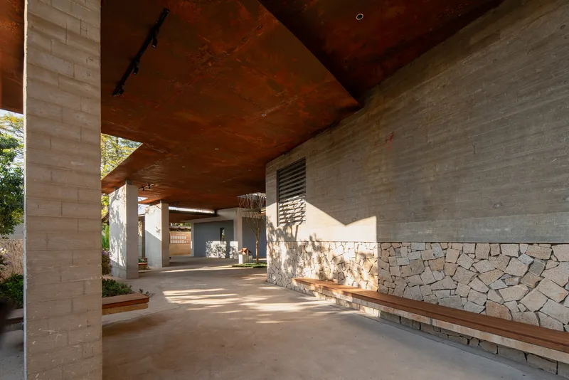 Covered walkway with weathered steel ceiling and stone and brick walls in afternoon light