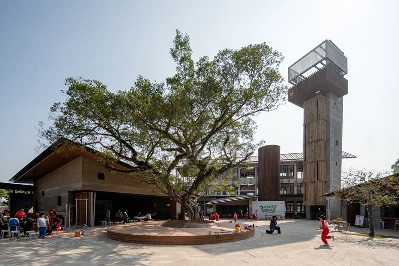 Central plaza with circular timber bench surrounding preserved tree and tower in background