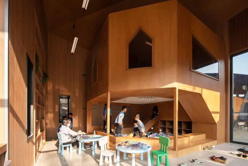 Double-height interior with plywood-clad volume and children at small tables below pendant lights