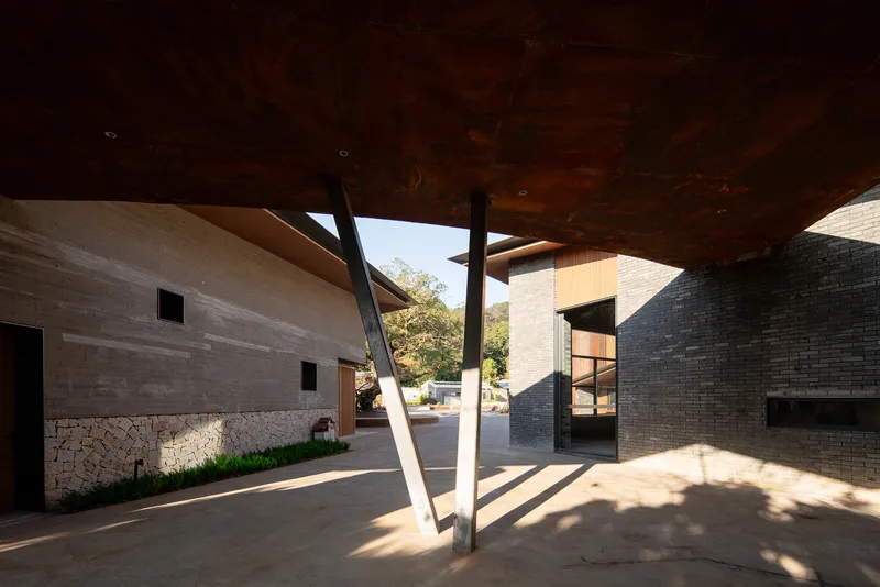 Covered courtyard plaza with angled steel columns supporting a timber soffit in morning sunlight