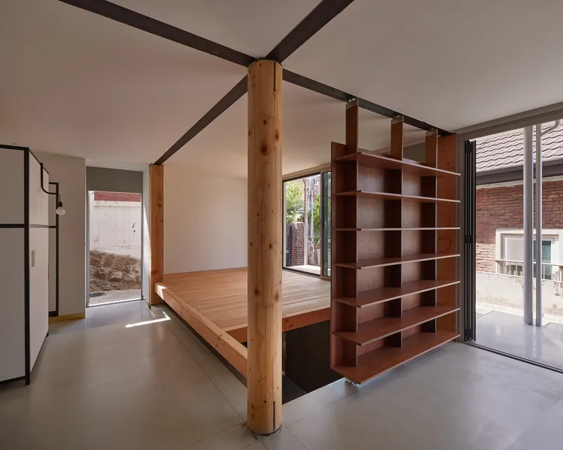 Open-plan interior with timber columns, steel beams, suspended timber platform and dark-stained shelving divider on concrete floor