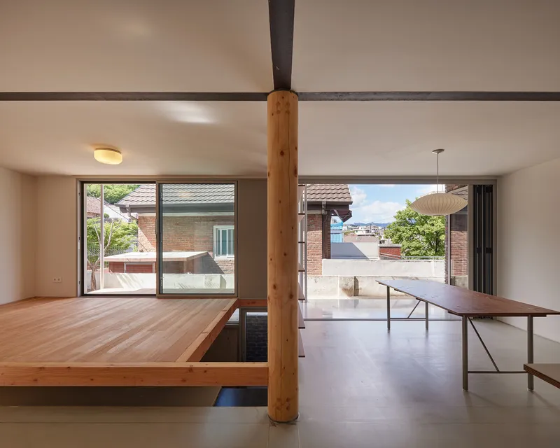 Split-level living space with raised timber platform beside a timber column and sliding glass doors opening to terrace