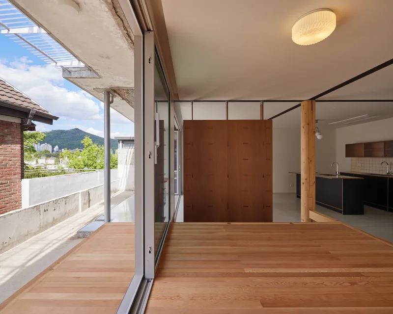 Interior view through sliding glass doors to the timber terrace with brise-soleil above and green mountains beyond