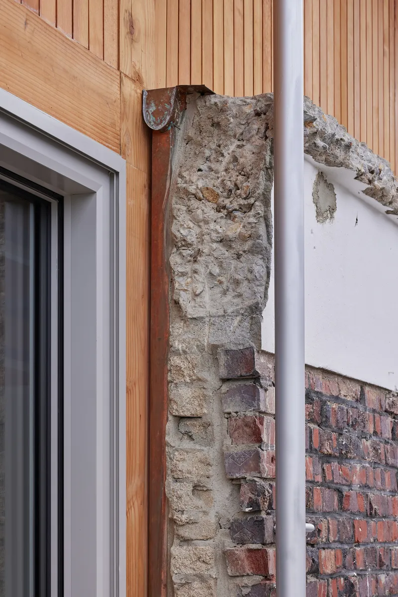 Close-up of exposed brick and concrete wall fragment adjoining new timber cladding and a white downpipe