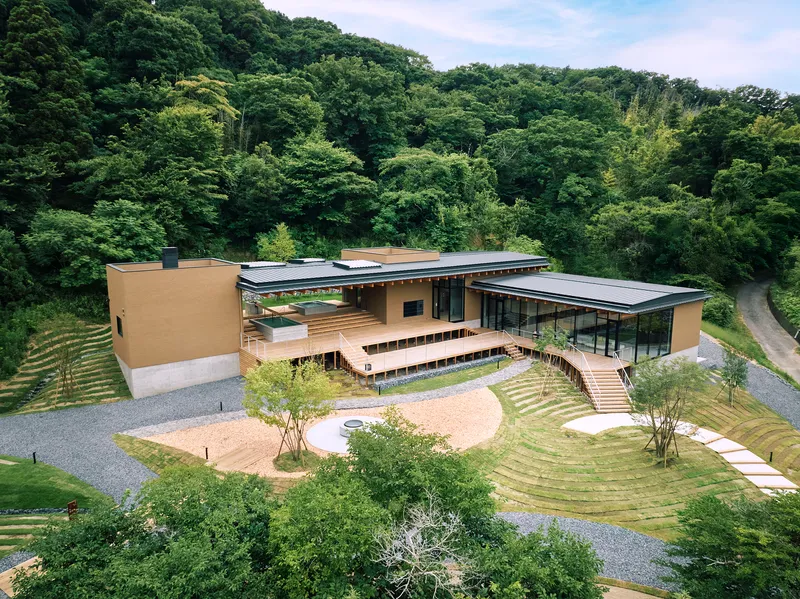 Aerial view of the low-lying compound with striped grass terraces nestled against a forested hillside