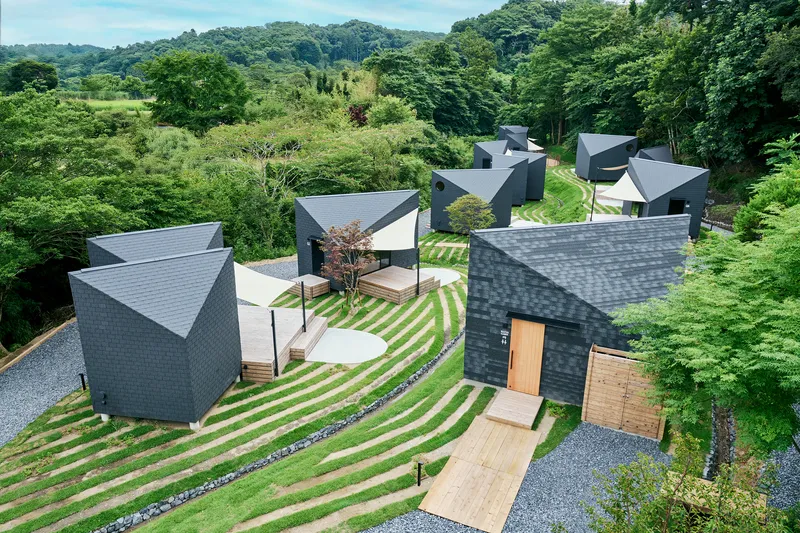Top-down view of the cluster of dark-tiled gable structures connected by pathways through striped lawn terraces