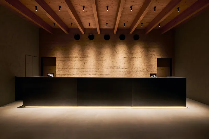 Reception desk with floating black volume and underlit base beneath exposed timber beams and downlights