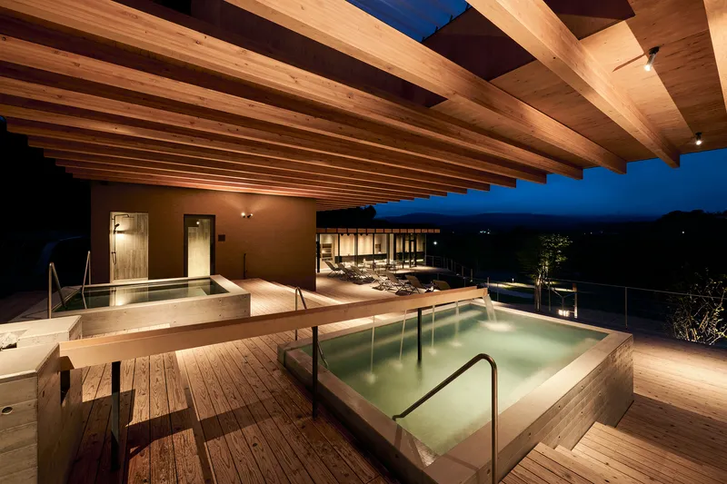 Rooftop terrace with soaking pools on timber decking under exposed beam canopy at dusk