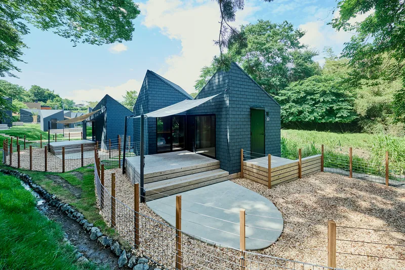 Dark timber-shingled facade with outdoor terrace, timber railings, and circular concrete pads on gravel