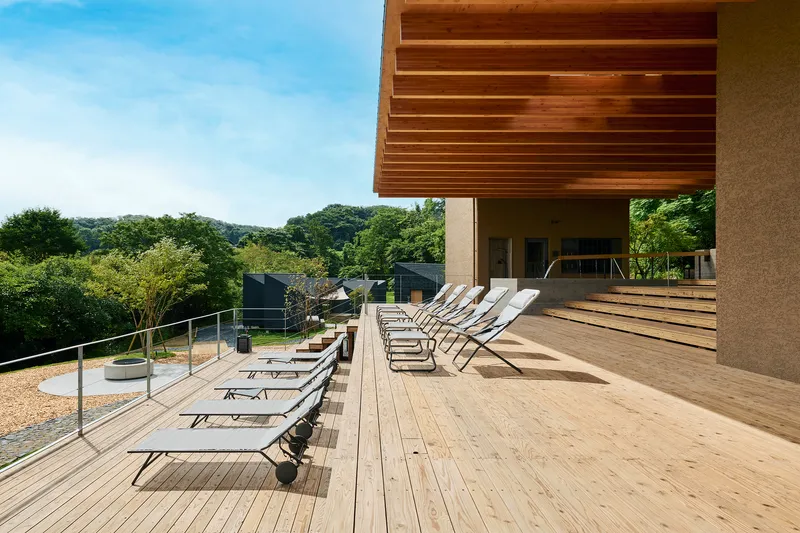 Timber deck terrace with canvas lounge chairs beneath a slatted wood canopy overlooking forested hills