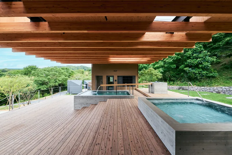 View beneath the timber beam canopy showing concrete spa pools and timber decking facing green valley