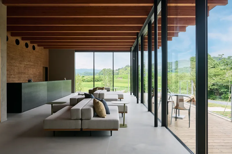 Open living space with exposed timber beam ceiling and full-height glazing overlooking green hills