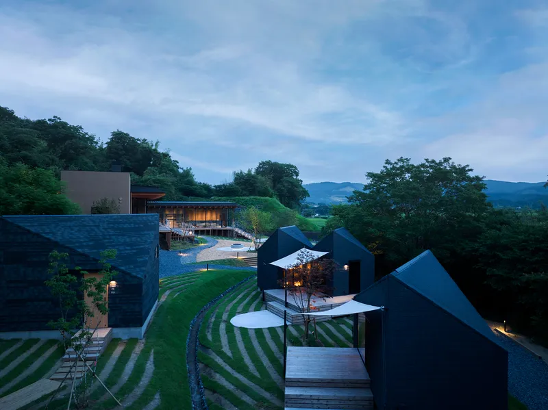 Aerial view at dusk showing dark gabled cabins arranged around terraced grass slopes