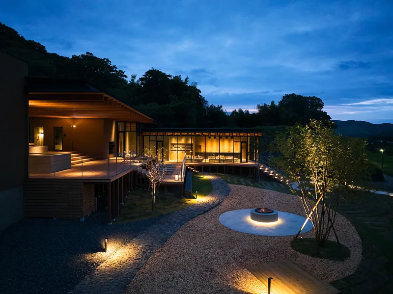 Glazed pavilion with timber deck and uplighting beneath a blue evening sky