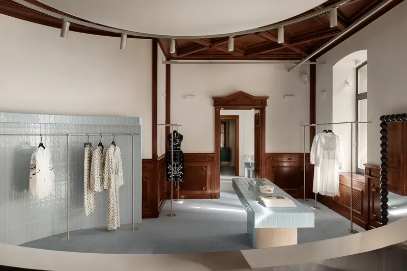 Retail interior with exposed dark timber beams, ribbed metal display tables and historic wood paneling