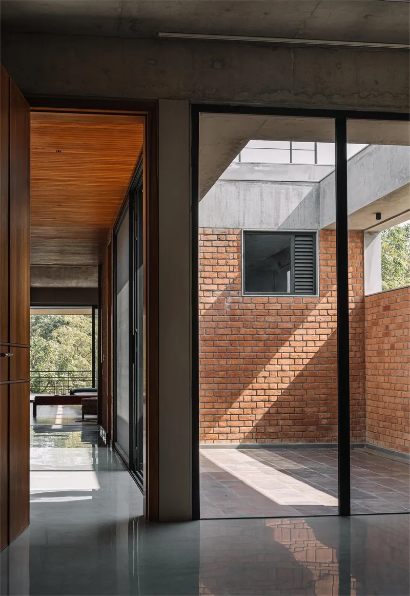 Interior corridor framed by exposed concrete ceiling and red brick courtyard wall catching afternoon sunlight