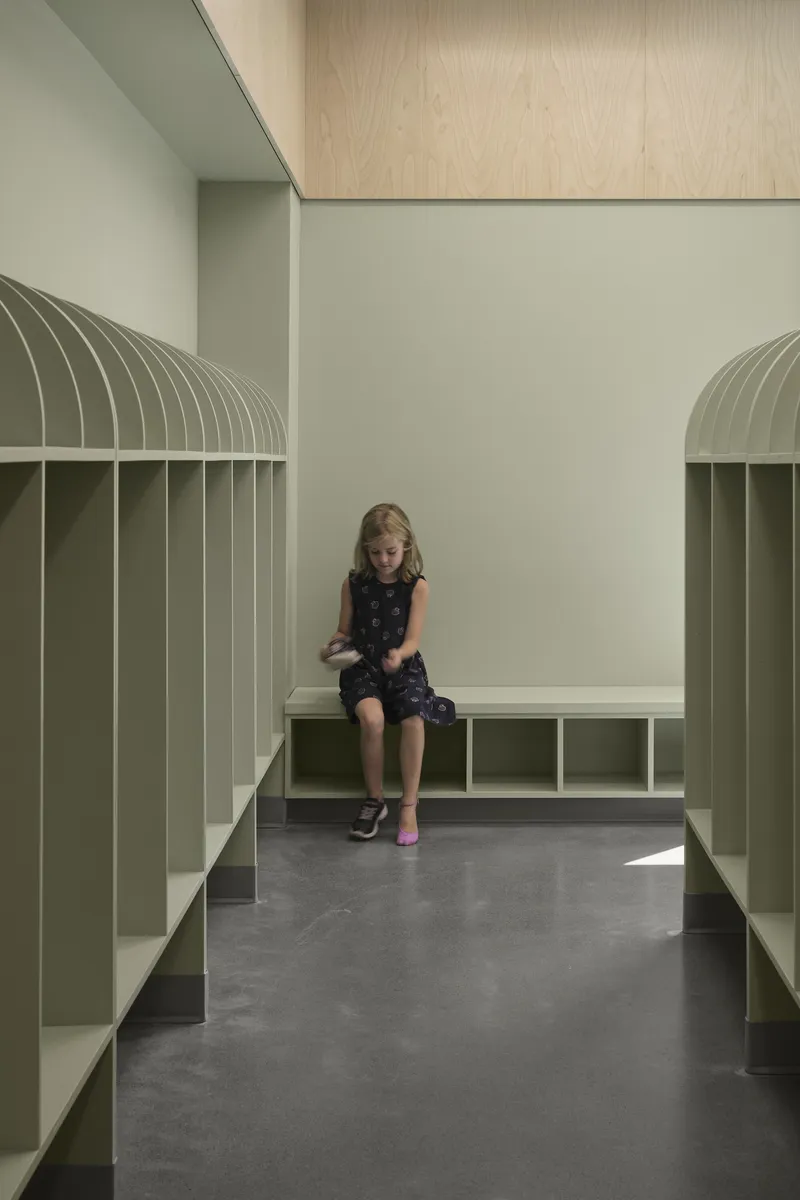 Interior storage nook with sage green arched cubbies and a child seated on the bench
