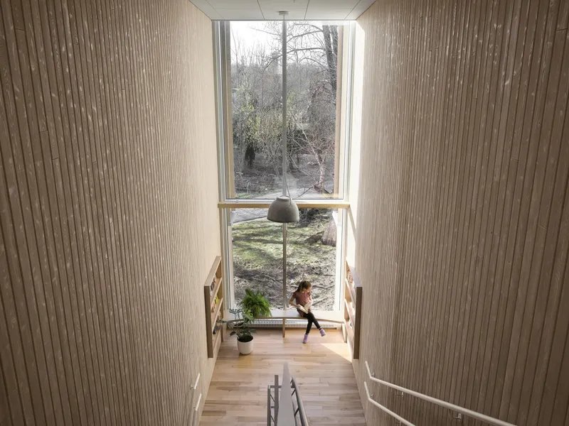 View down a timber staircase toward a tall window framing bare winter trees and a figure below