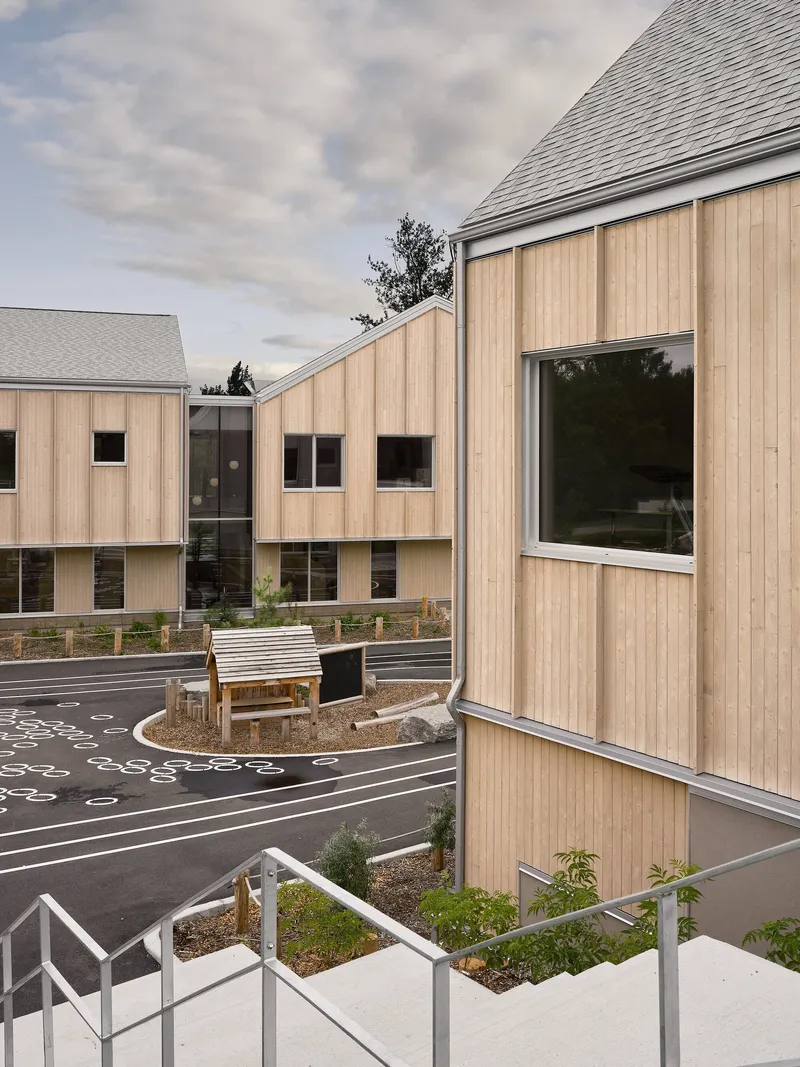 Elevated view of timber gables surrounding a patterned courtyard with planted beds and a timber bench