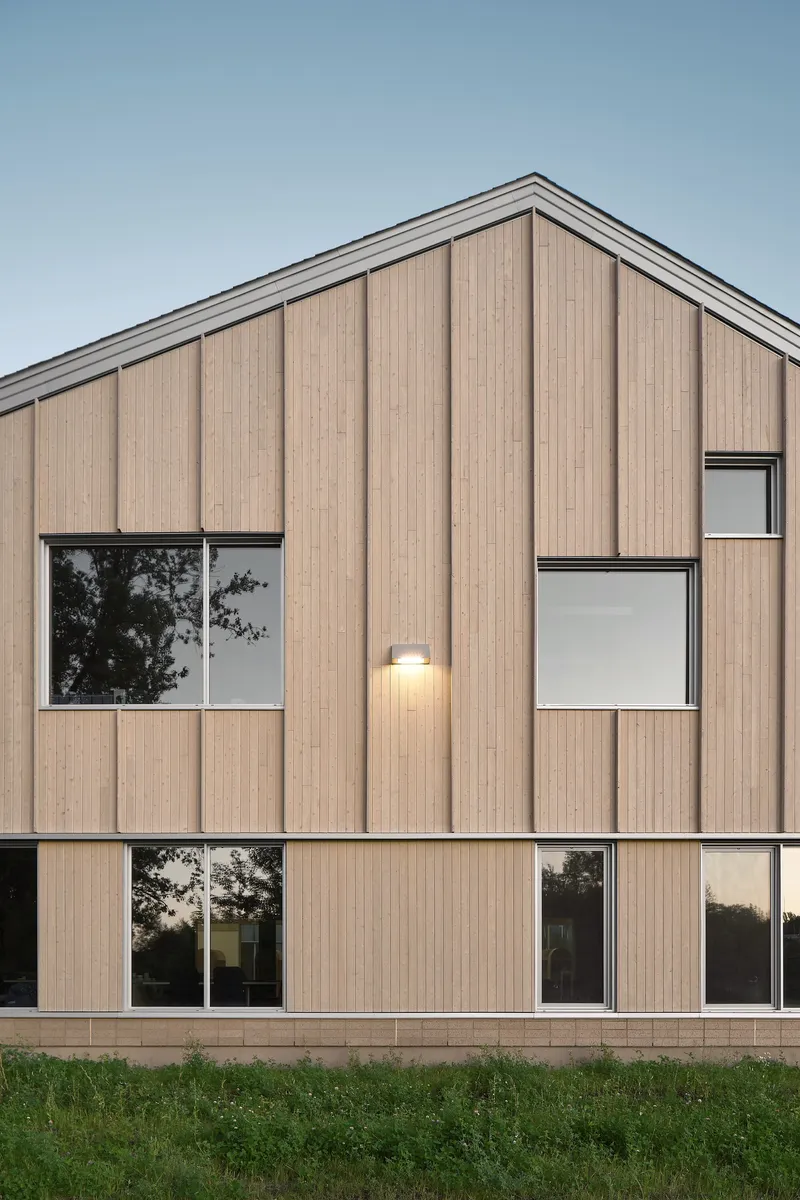 Two-story timber facade with scattered punched windows and an exterior wall light at dusk
