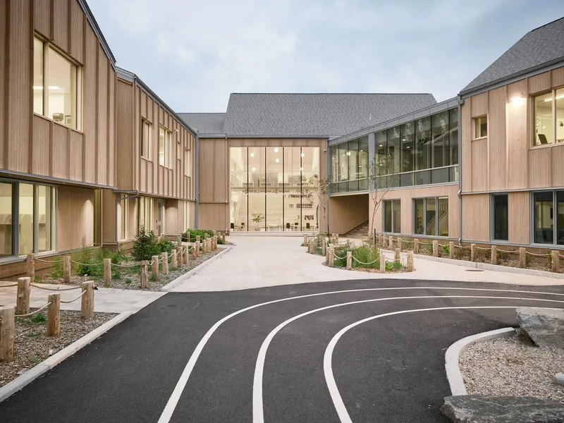 Central entrance with glazed facade and timber wings framing a curved asphalt path at twilight