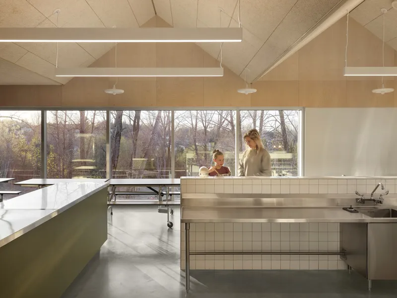 Kitchen with white tile backsplash and plywood ceiling panels overlooking bare trees through horizontal windows