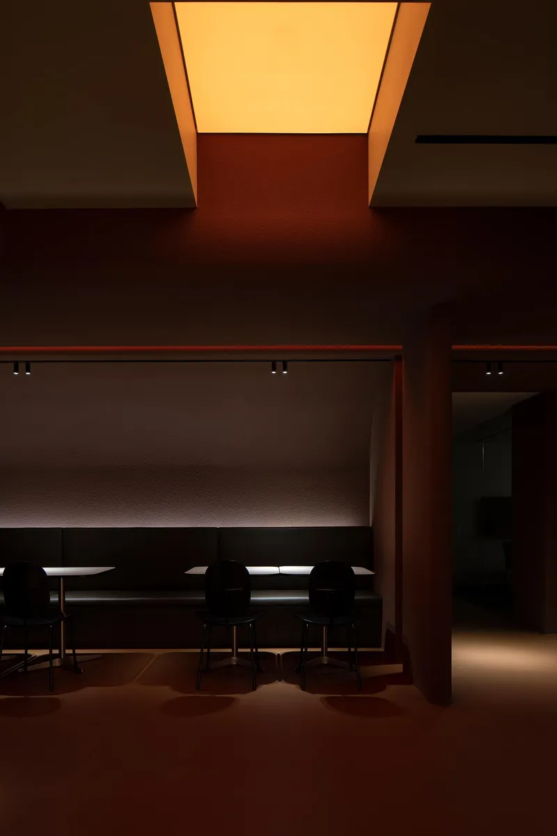 Dining area with long table beneath a recessed illuminated ceiling panel casting amber glow