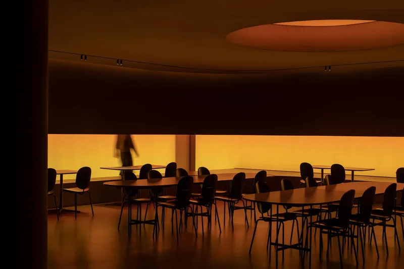 Dining area with curved ceiling oculus and backlit amber translucent wall panel with a figure passing