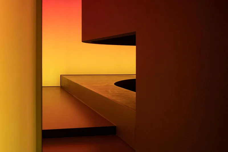 Geometric timber bench and steps beneath a glowing yellow wall panel in a recessed alcove