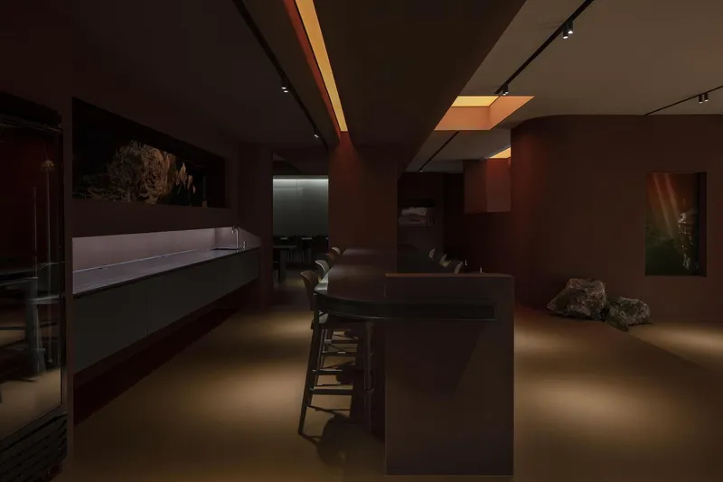 Gallery space with brown walls, display cases, and amber skylight strips illuminating the ceiling