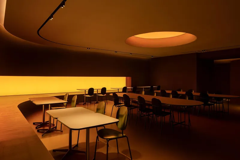 Dining area with curved ceiling featuring an oval skylight and backlit horizontal window in warm lighting