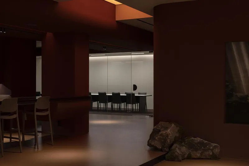 View through terracotta portal toward conference room with backlit translucent panels and raw stone on floor