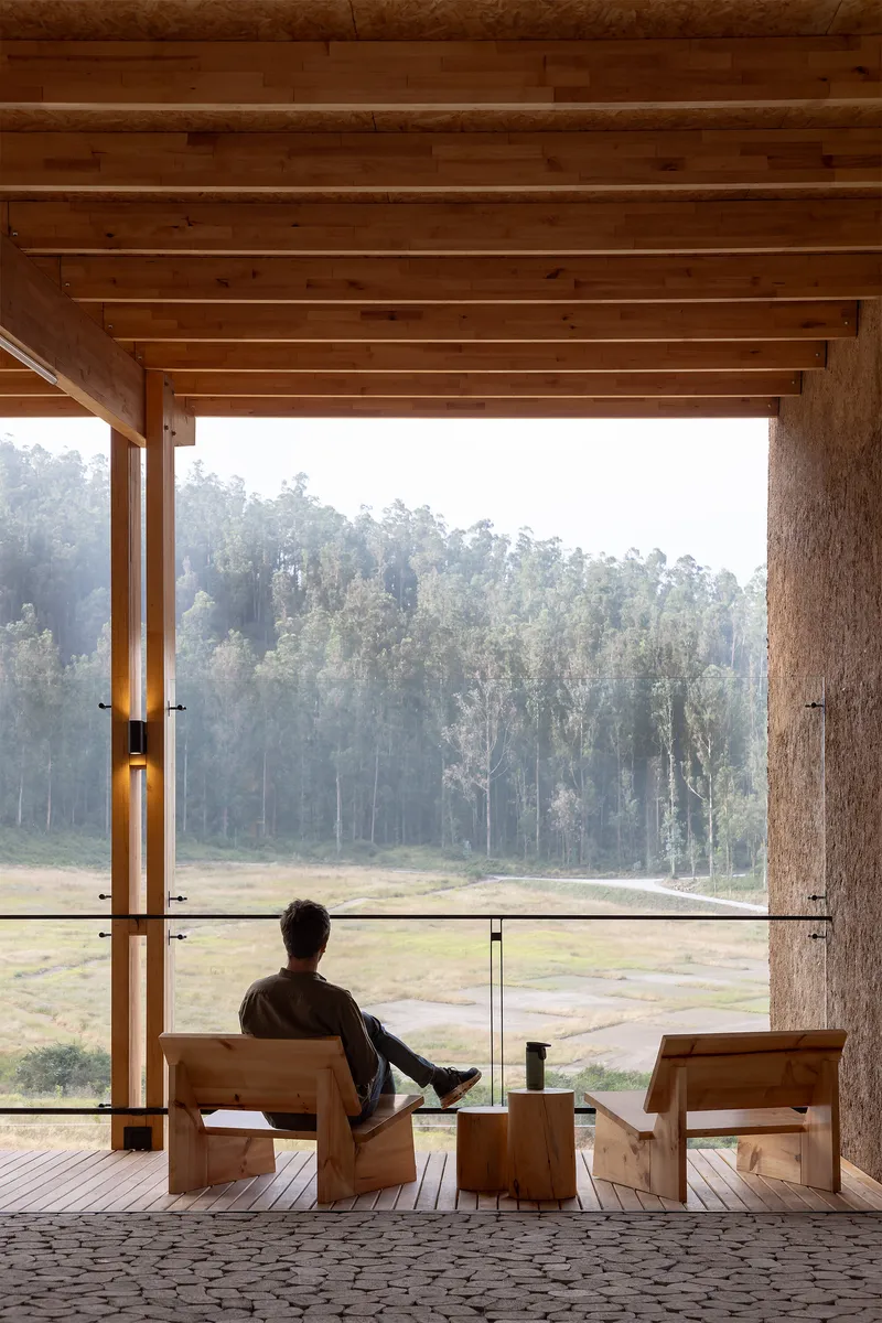 Covered veranda with exposed timber beams and person seated on wooden furniture overlooking misty fields