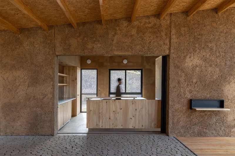 View from textured panel room through doorway to kitchen counter with person in motion inside