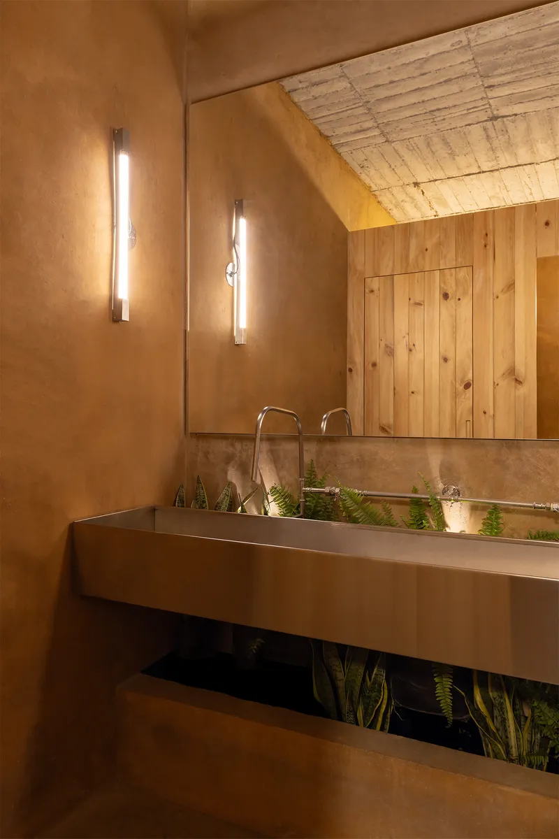 Bathroom vanity with steel trough sink and vertical sconces flanking a timber-lined mirror under an exposed plank ceiling