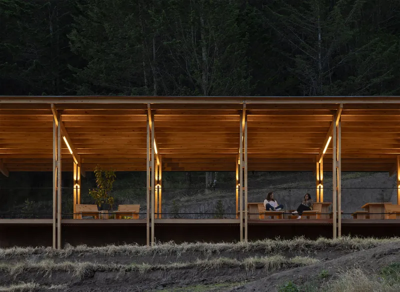 Glazed facade with timber columns and slatted soffit at dusk with two figures seated inside